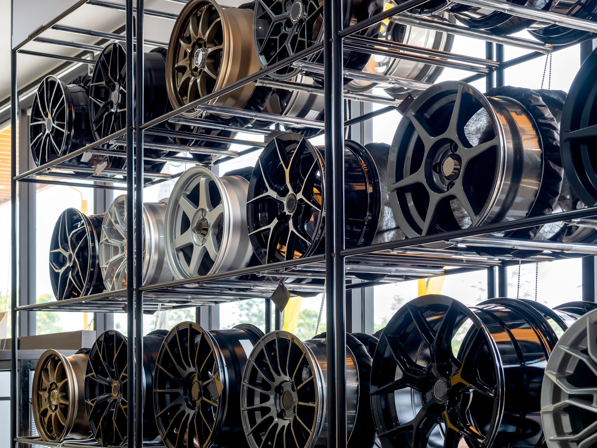 Szene der modernen Reifenladendekoration mit verschiedenen Designs von Stahllegierungsrädern auf Metallregal im Inneren des Gebäudes in der Nähe eines riesigen Glasfensters. Hintergrund des Showroom-Shops für Leichtmetallfelgen.