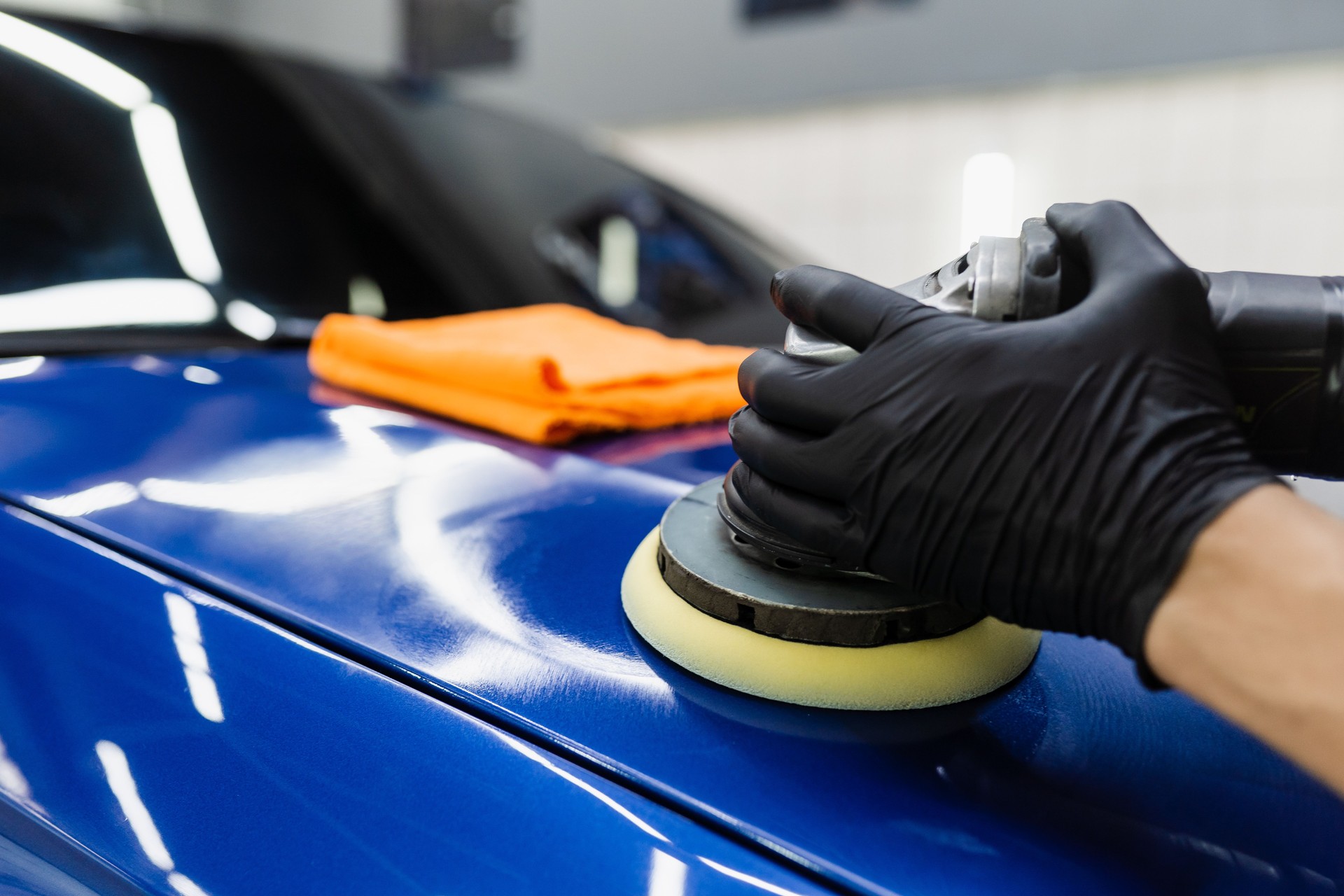 Dichtstoff-Autopolitur mit Orbitalpolierer zum Entfernen von Kratzern. Arbeiter der Detaillierung Auto-Service, der das letzte Polieren für das Auto macht.